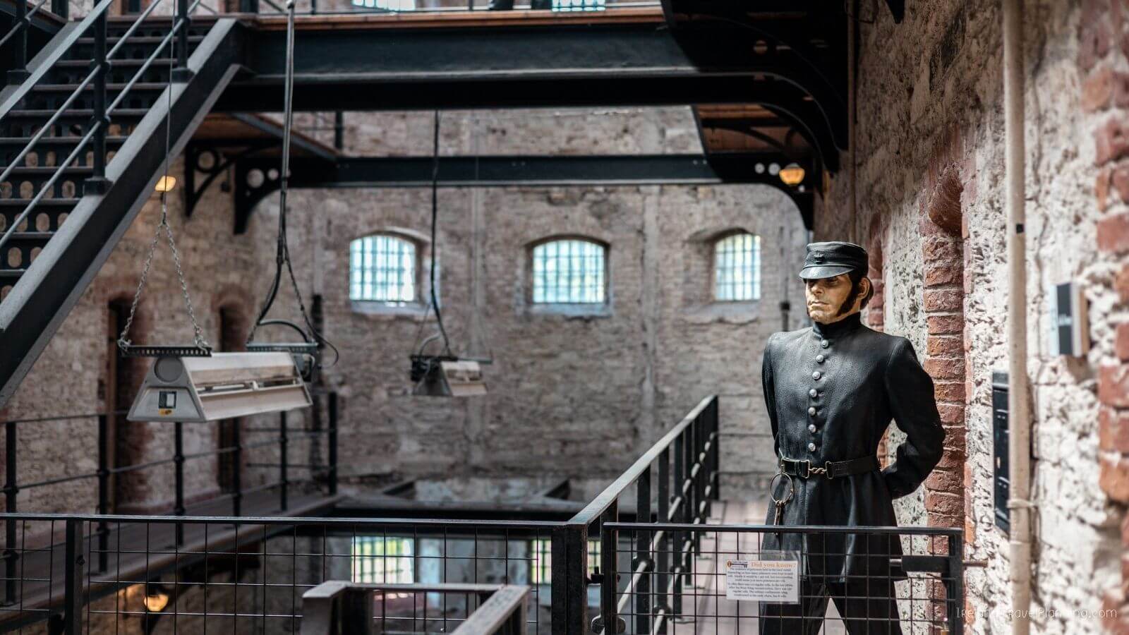 Statue of a guard in the old Cork City Jail with brick walls and hanging lamps