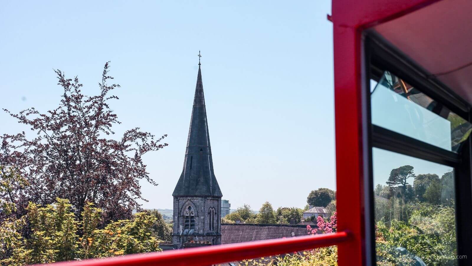 View of a steeple from inside a red vehicle with trees and houses in background