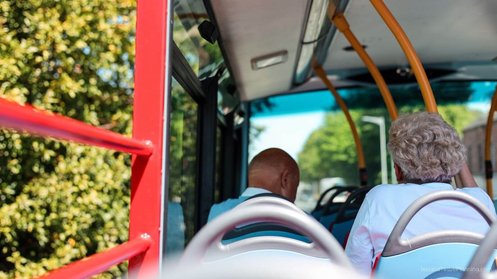 Two people sitting inside a red bus with trees outside the window
