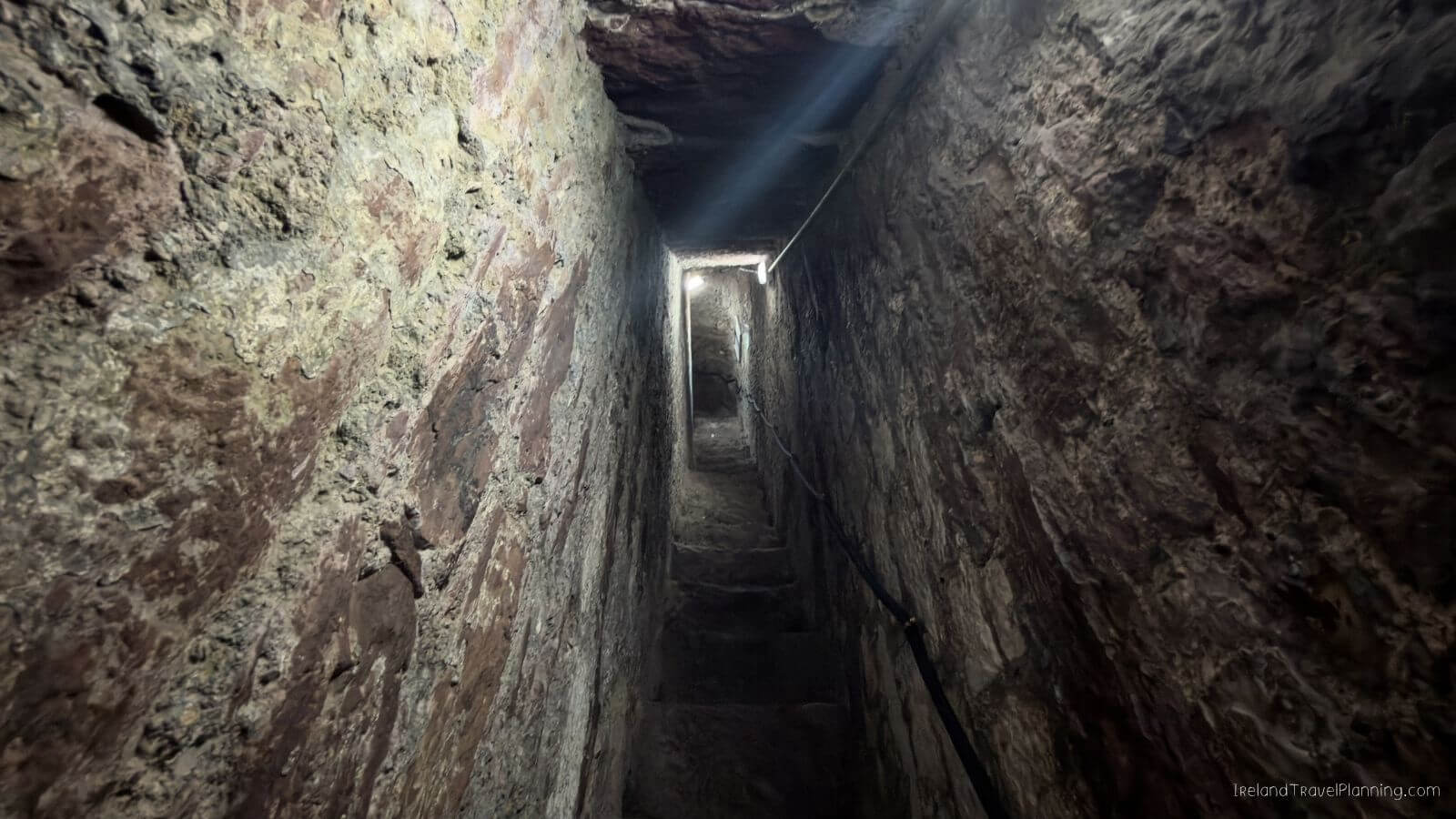 Steep stone staircase leading up to a bright exit in a narrow passageway