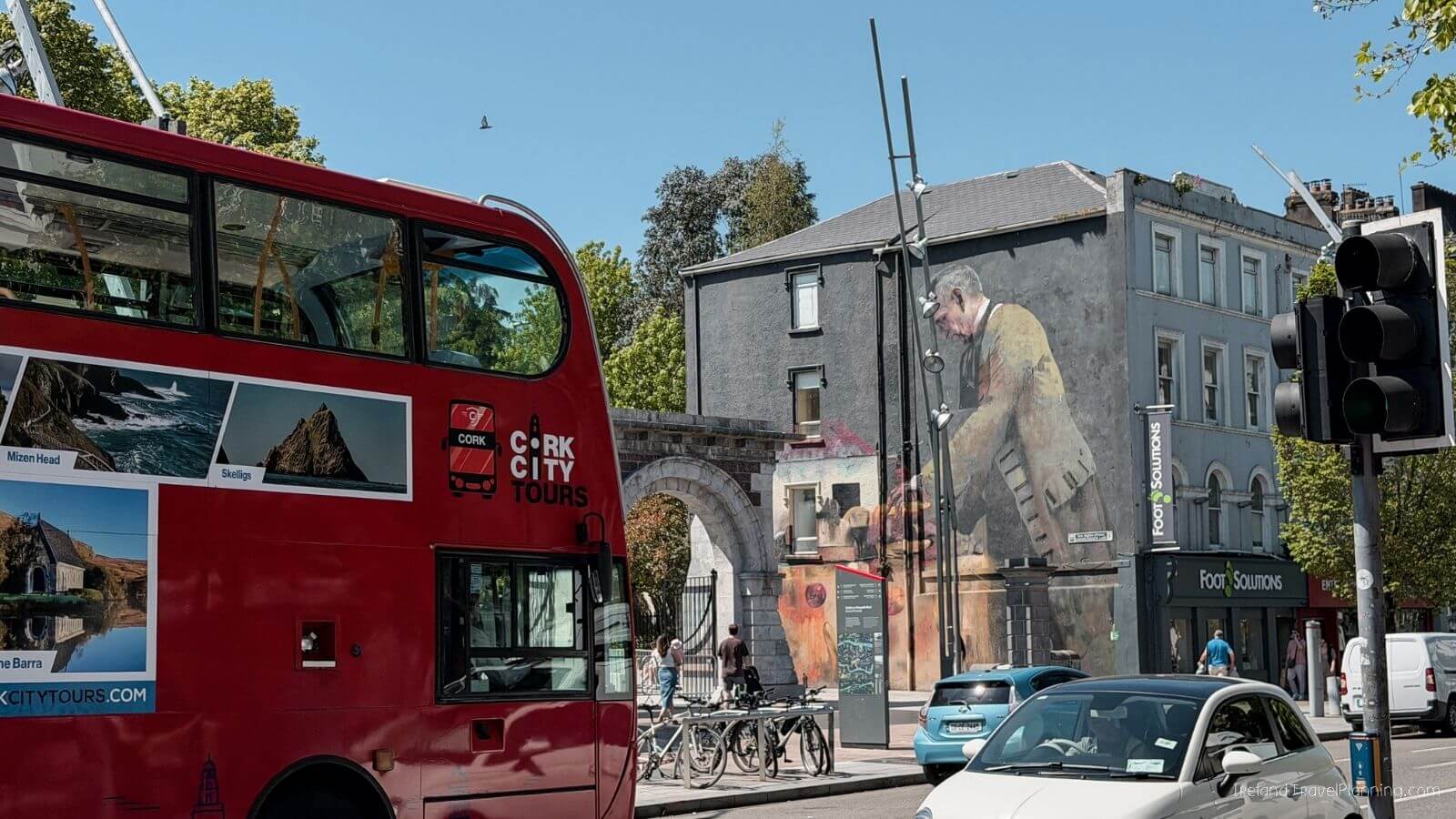 Red Cork City Tours bus parked near a mural in Cork, Ireland.