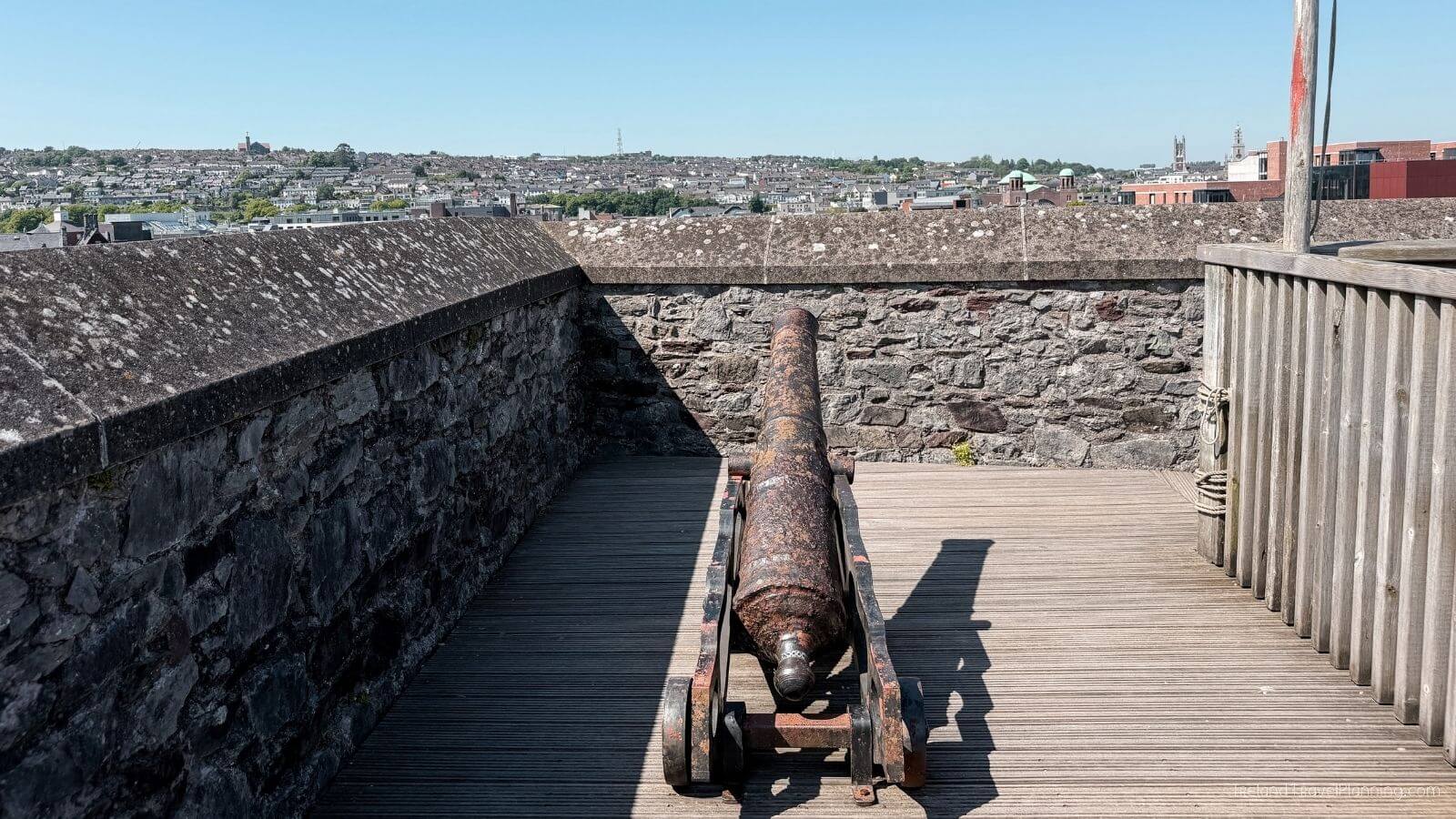 Old cannon on a wooden deck with a stone wall overlooking Cork City