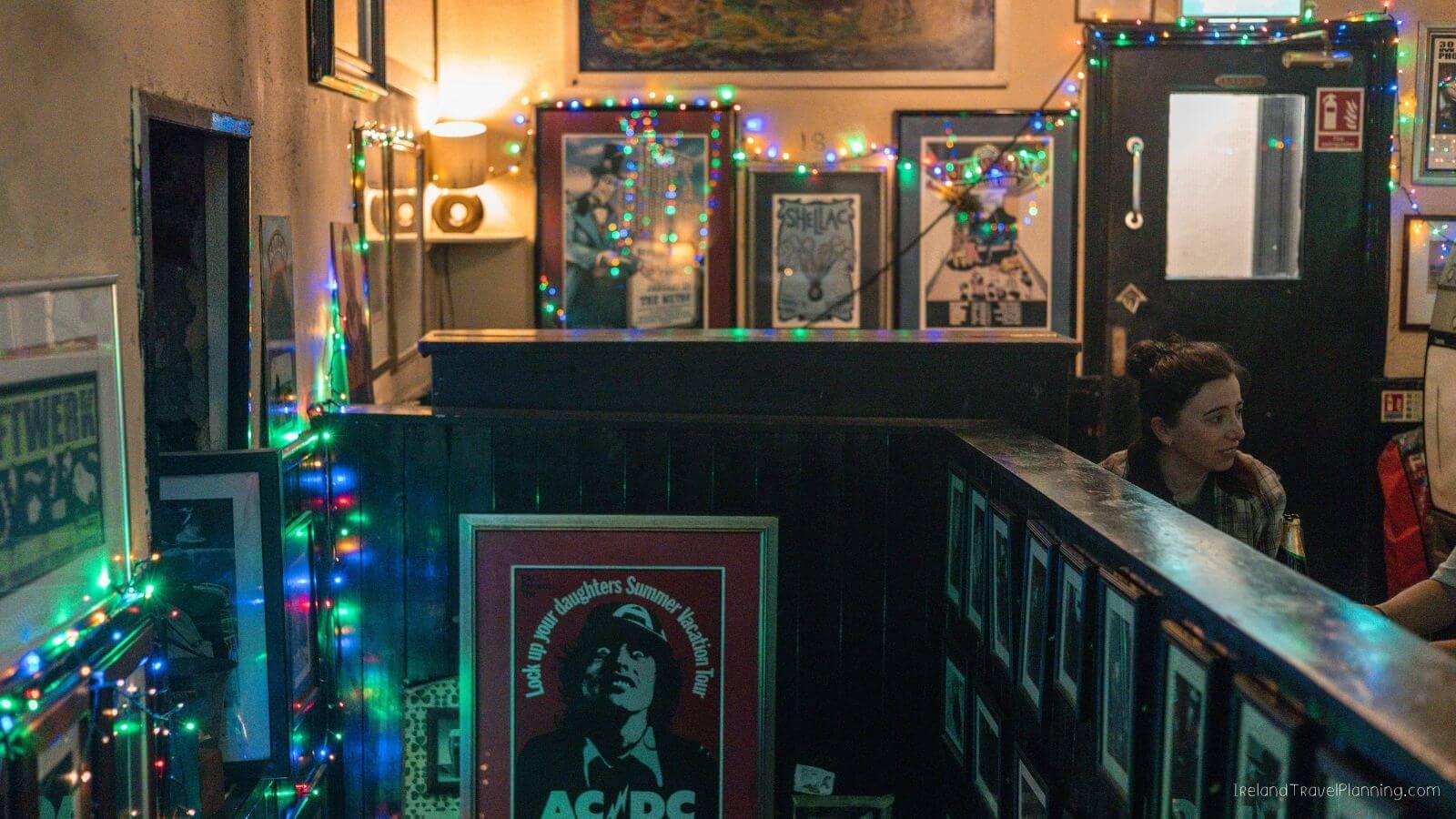 Cork City pub interior with ACDC poster, woman sitting, Christmas lights