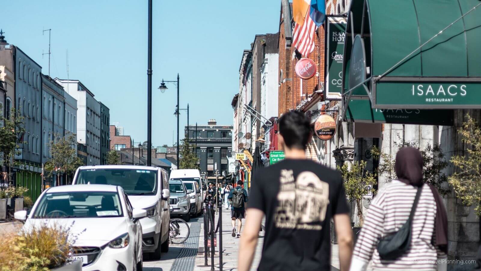 People walking past shops in Cork City with parked cars on the street