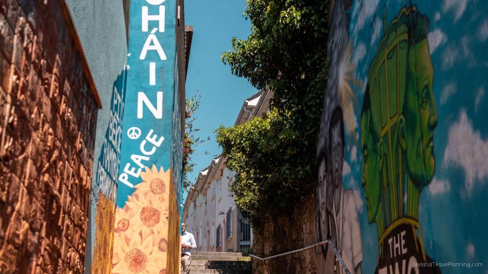Narrow alley in Cork City with colorful murals including "CHAIN PEACE" and a man walking