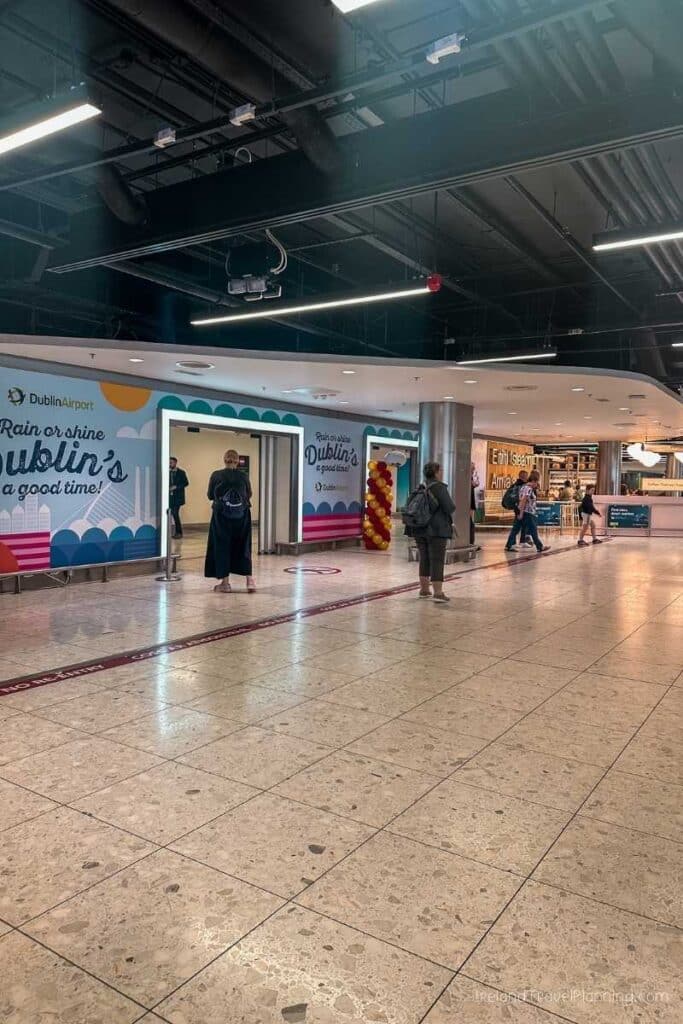 Dublin Airport arrivals hall with colorful "Rain or shine Dublin's a good time!" banner.