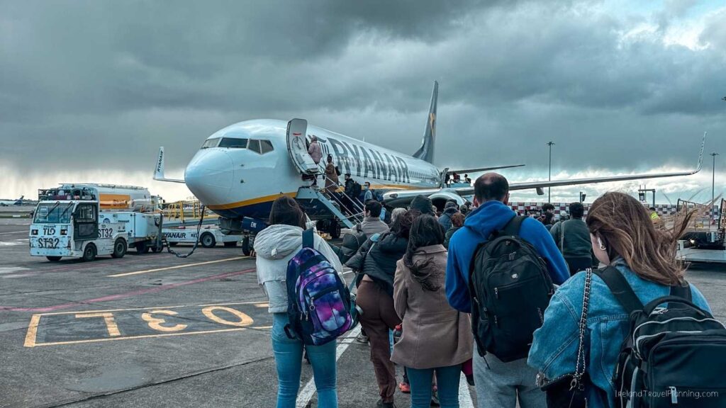 Ryanair plane boarding with passengers queuing on the tarmac under a cloudy sky.