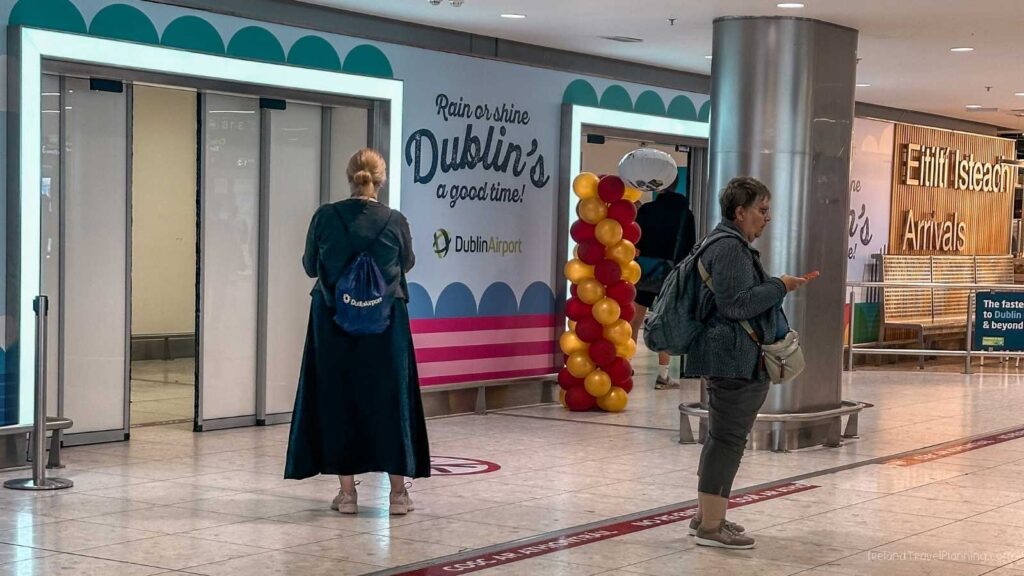 Dublin Airport arrivals hall with people and a balloon arch.