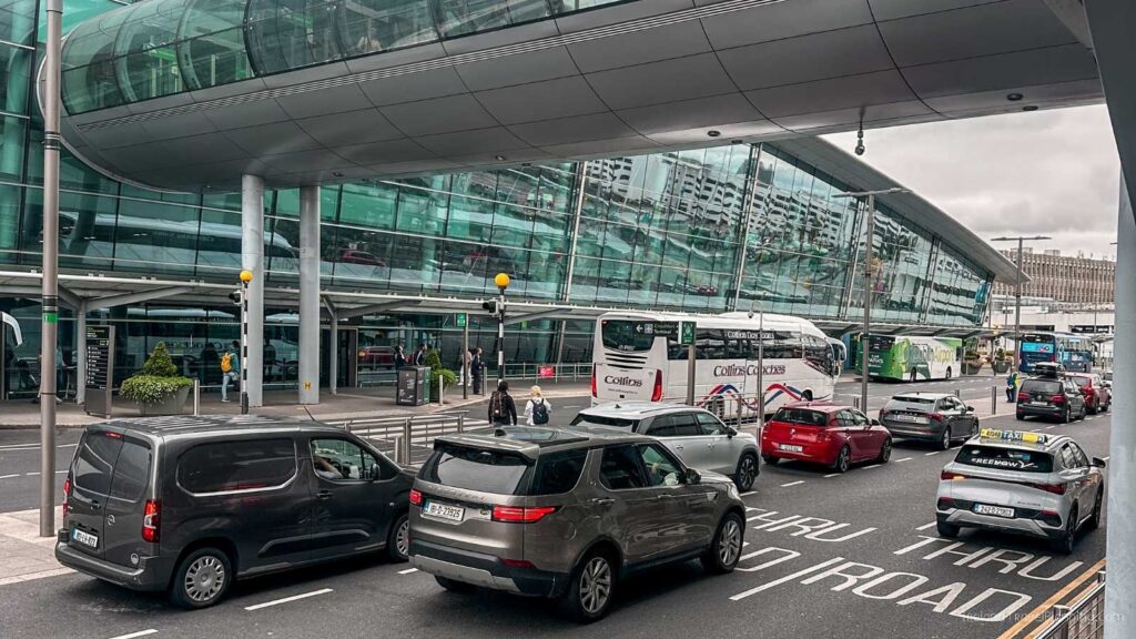 Busy airport drop-off zone with cars, buses, and modern terminal building