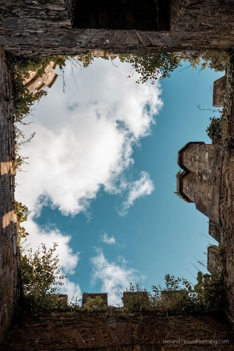 Looking up through ancient Irish castle ruins at a blue sky with white clouds