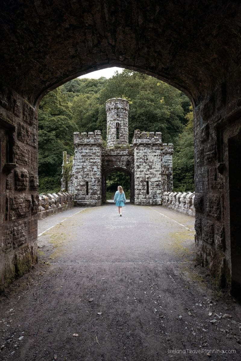 Woman walks through stone archway towards abandoned castle ruins in Ireland