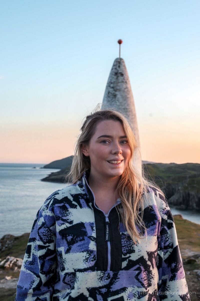 Young woman in fleece jacket at coastal landmark during sunset