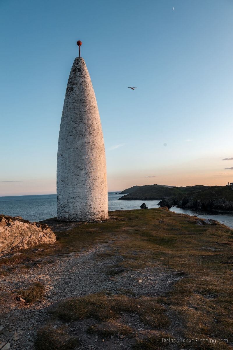 Conical marker on a grassy cliff overlooking the sea at sunset, Ireland