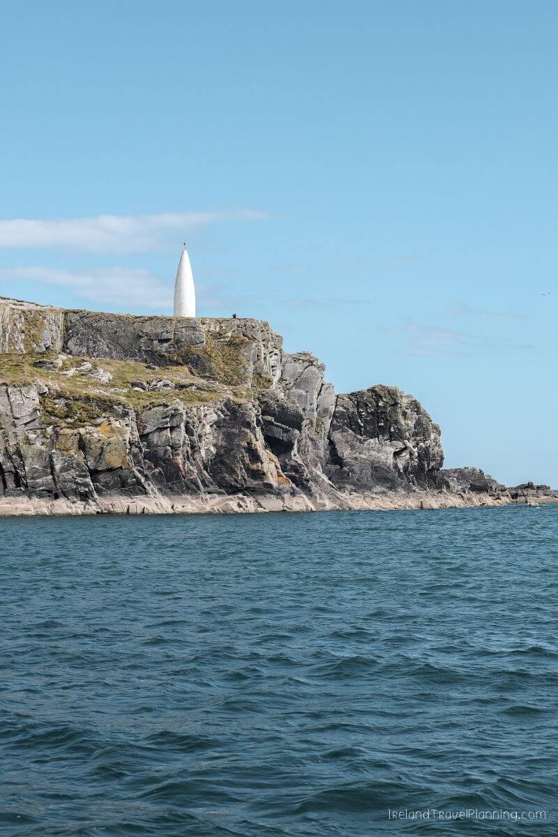 White spire on rocky cliff overlooking the sea, a hidden gem in Ireland.