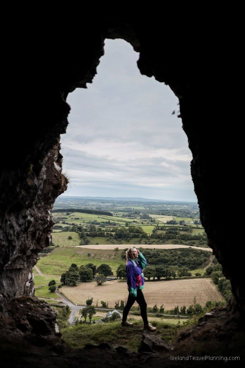 Woman looking out from a cave at the rolling green hills of Ireland.
