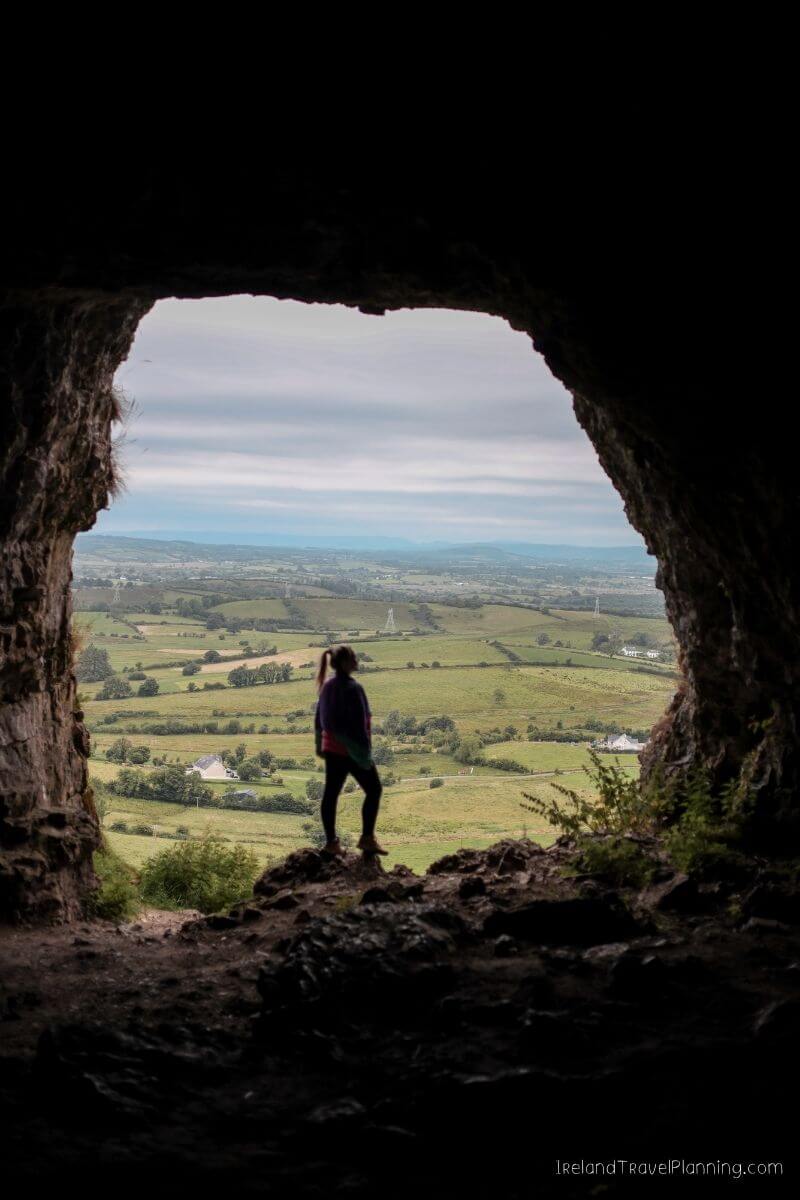Woman looking out from a cave at the green Irish countryside.