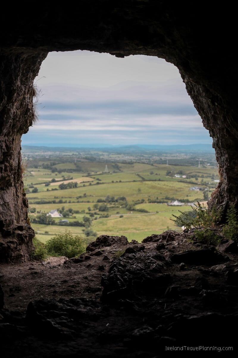 View from a cave in Ireland overlooking rolling green fields and distant hills.