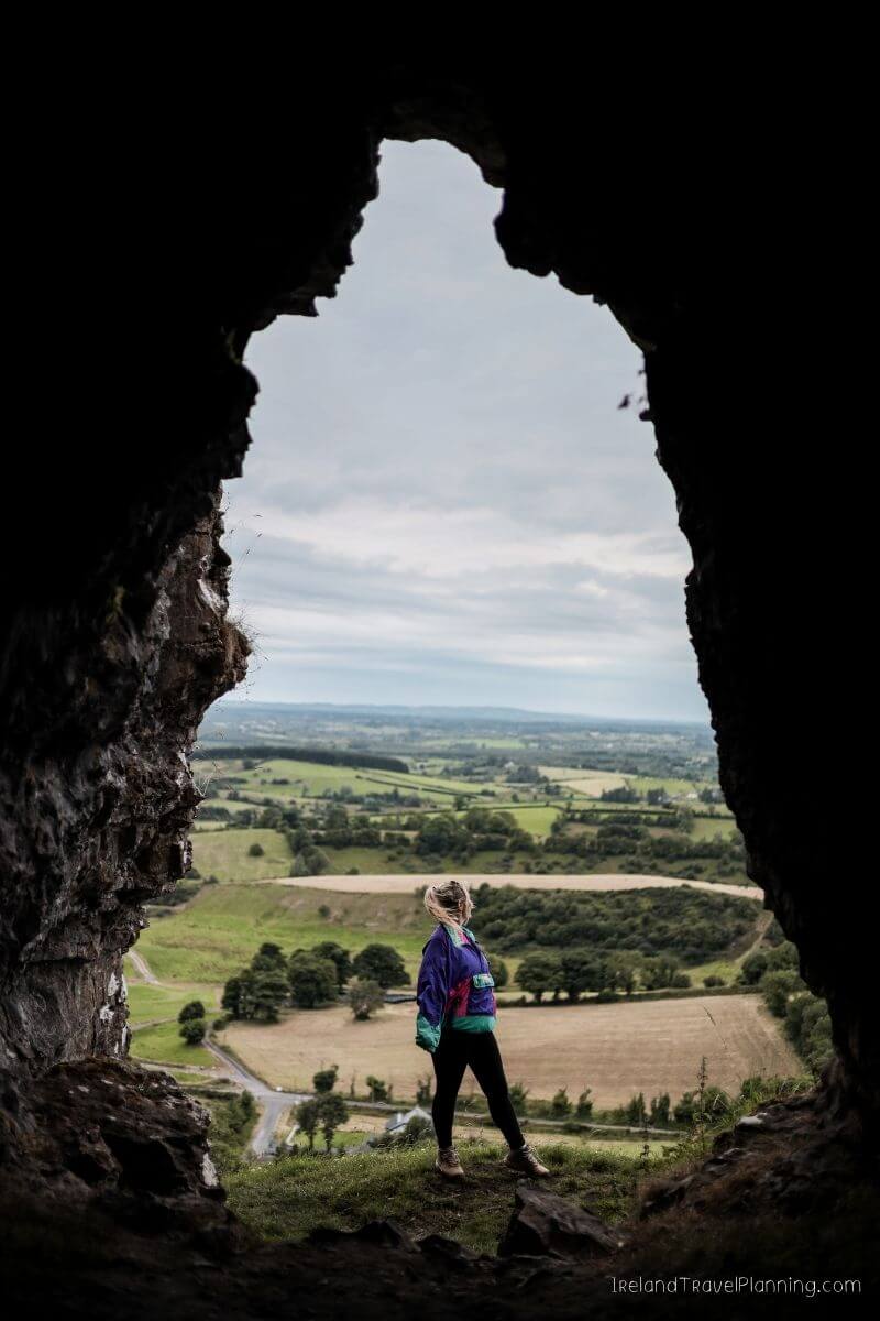 Woman overlooking rolling green hills from a cave in Ireland