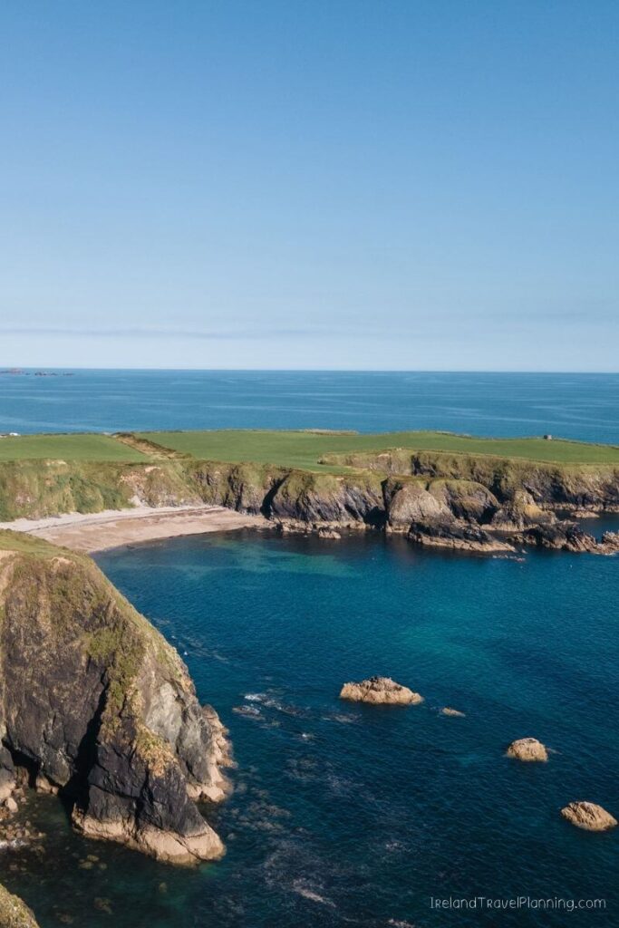 Rugged Irish coastline with a hidden cove and lush green cliffs overlooking the Atlantic Ocean.
