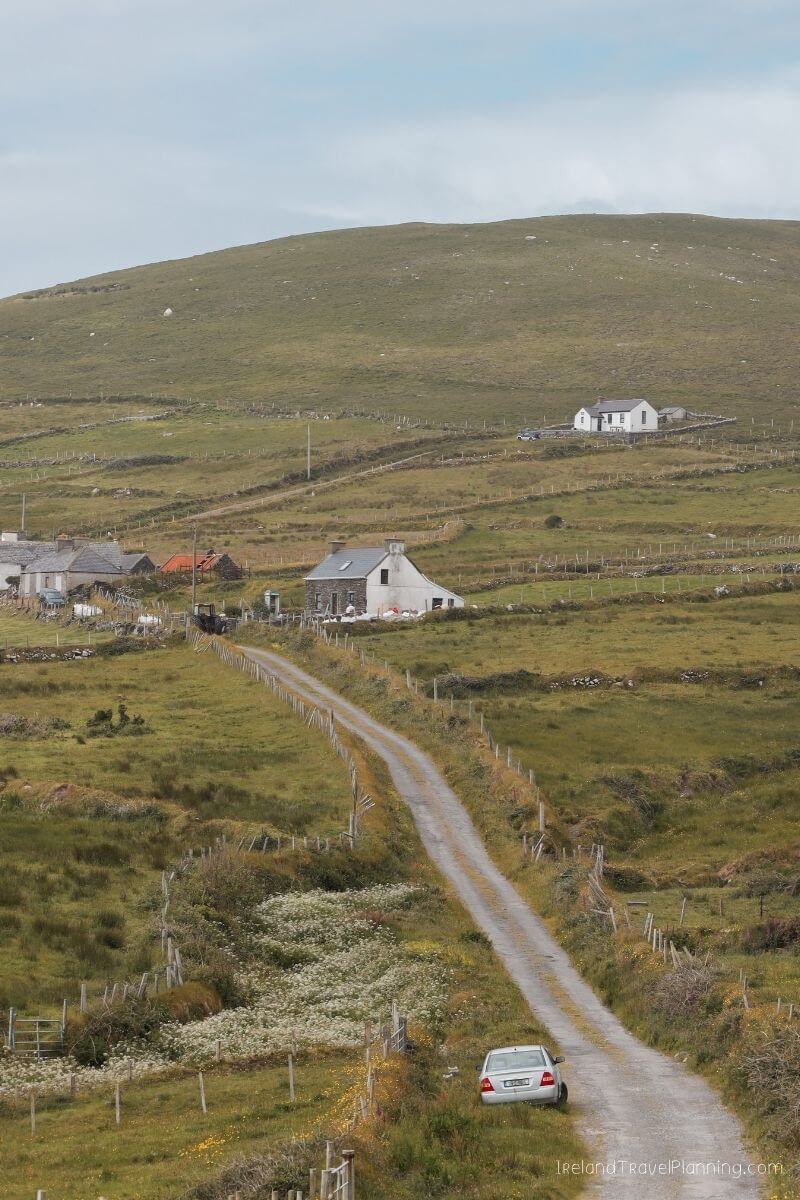 Car parked on rural road with Irish cottages in the distance