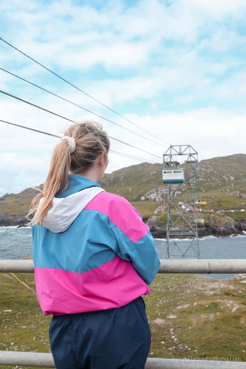 Woman in colorful jacket looks at Dursey Island cable car, Ireland.