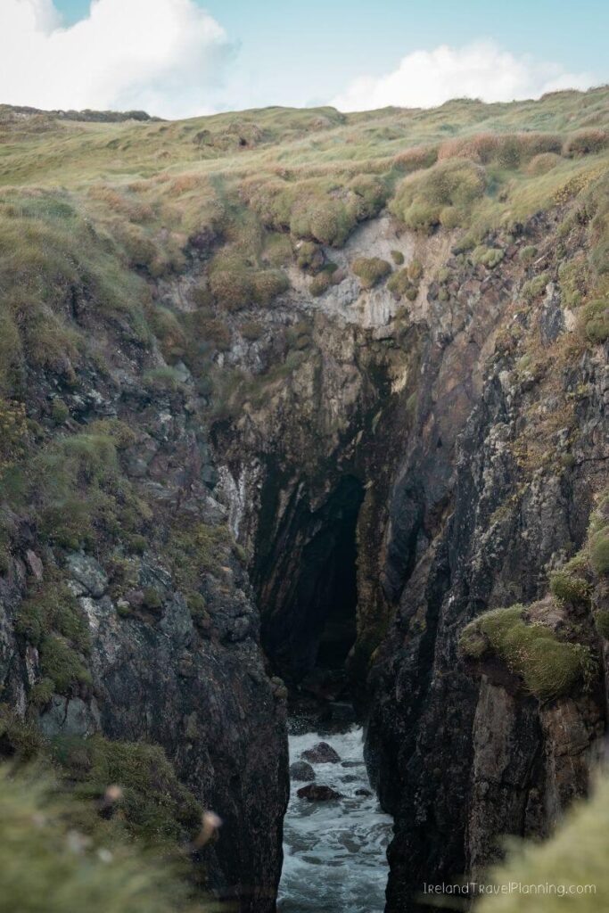 Dramatic sea cave with waves crashing into a narrow opening on the Irish coast.