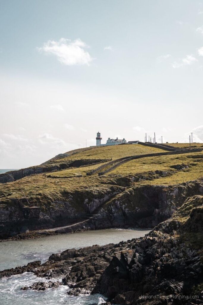 Lighthouse on a grassy Irish cliffside overlooking the sea, with stone walls