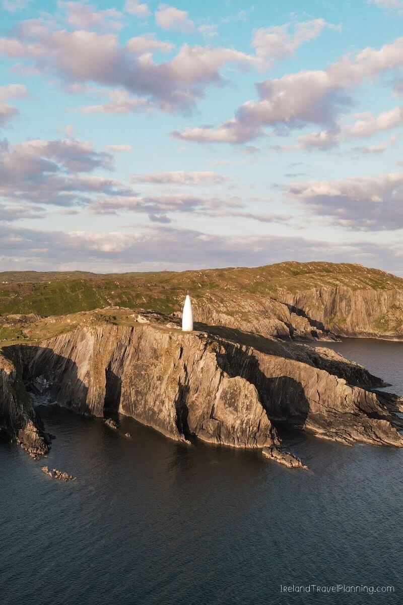 White lighthouse on a rocky cliff overlooking the ocean under a cloudy sky.