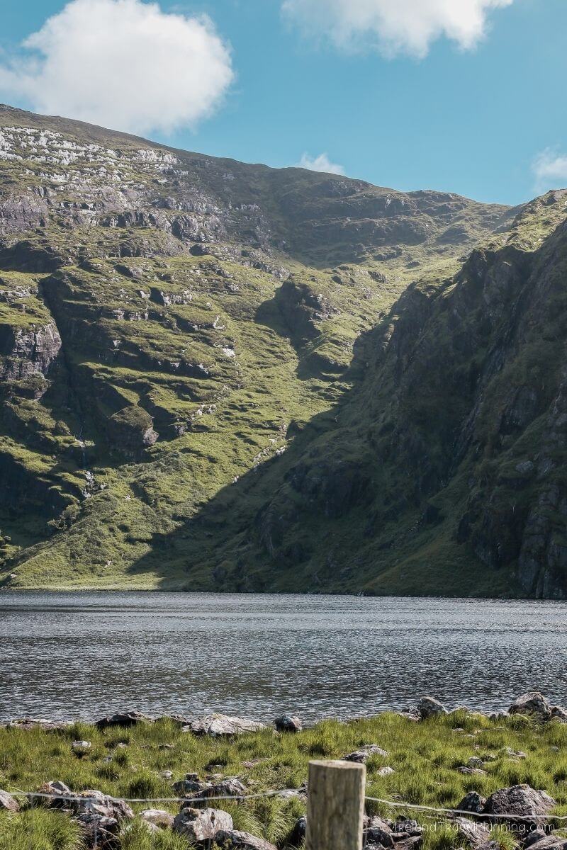Serene lake nestled beneath a lush, green Irish mountainside.