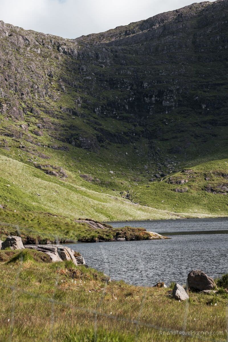 Rugged Irish mountainside slopes down to a dark, calm lake, a hidden gem.