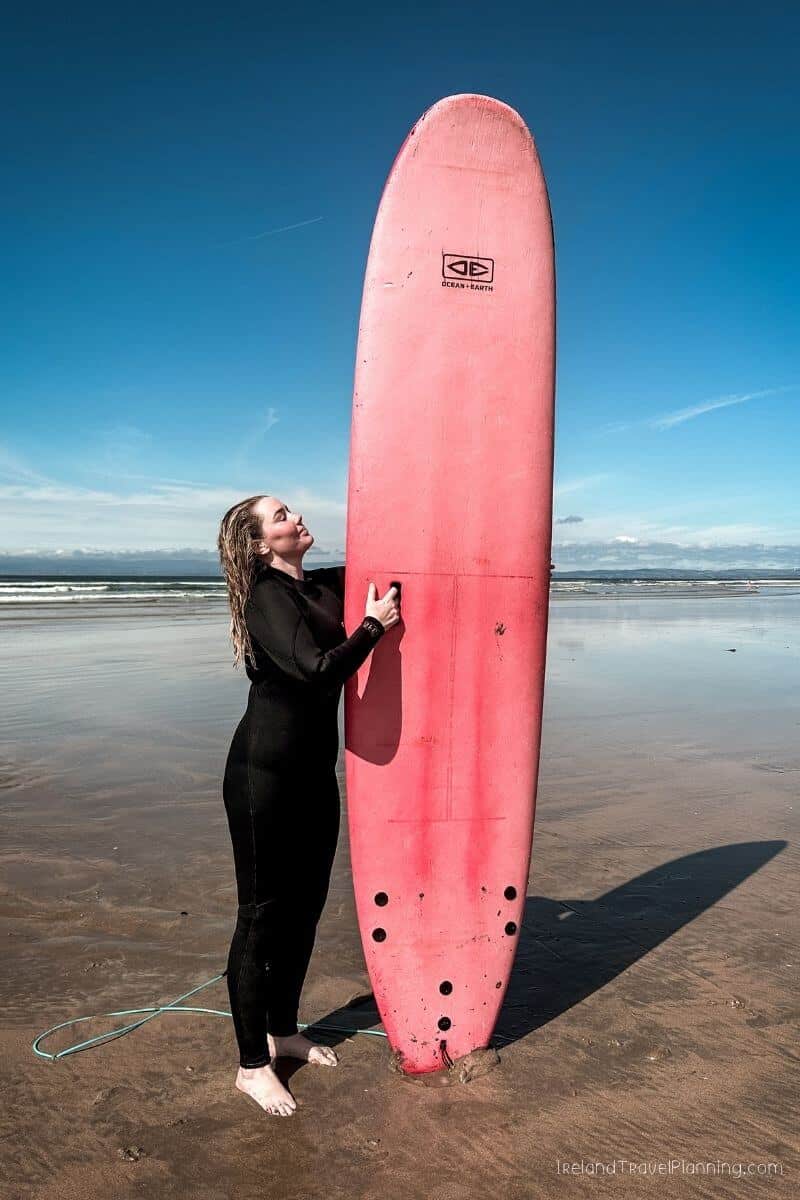Woman in wetsuit with pink surfboard on beach