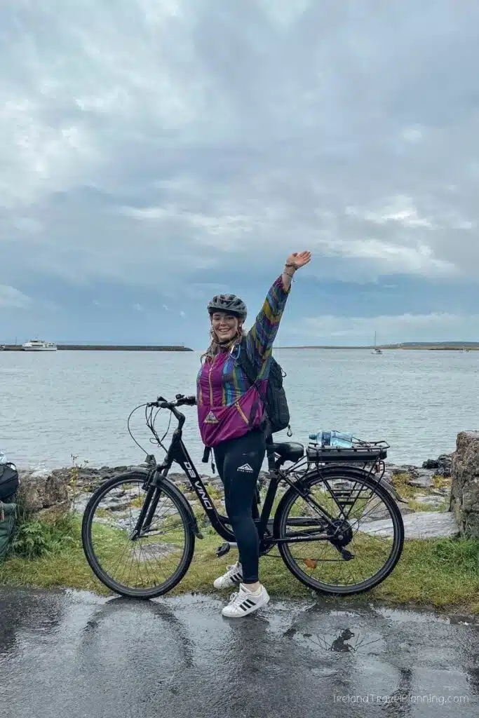 Woman with bicycle waves hello by the sea in Ireland