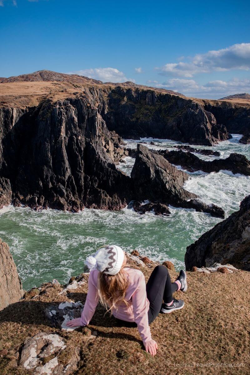 Woman on cliff overlooking rugged coastline and ocean waves