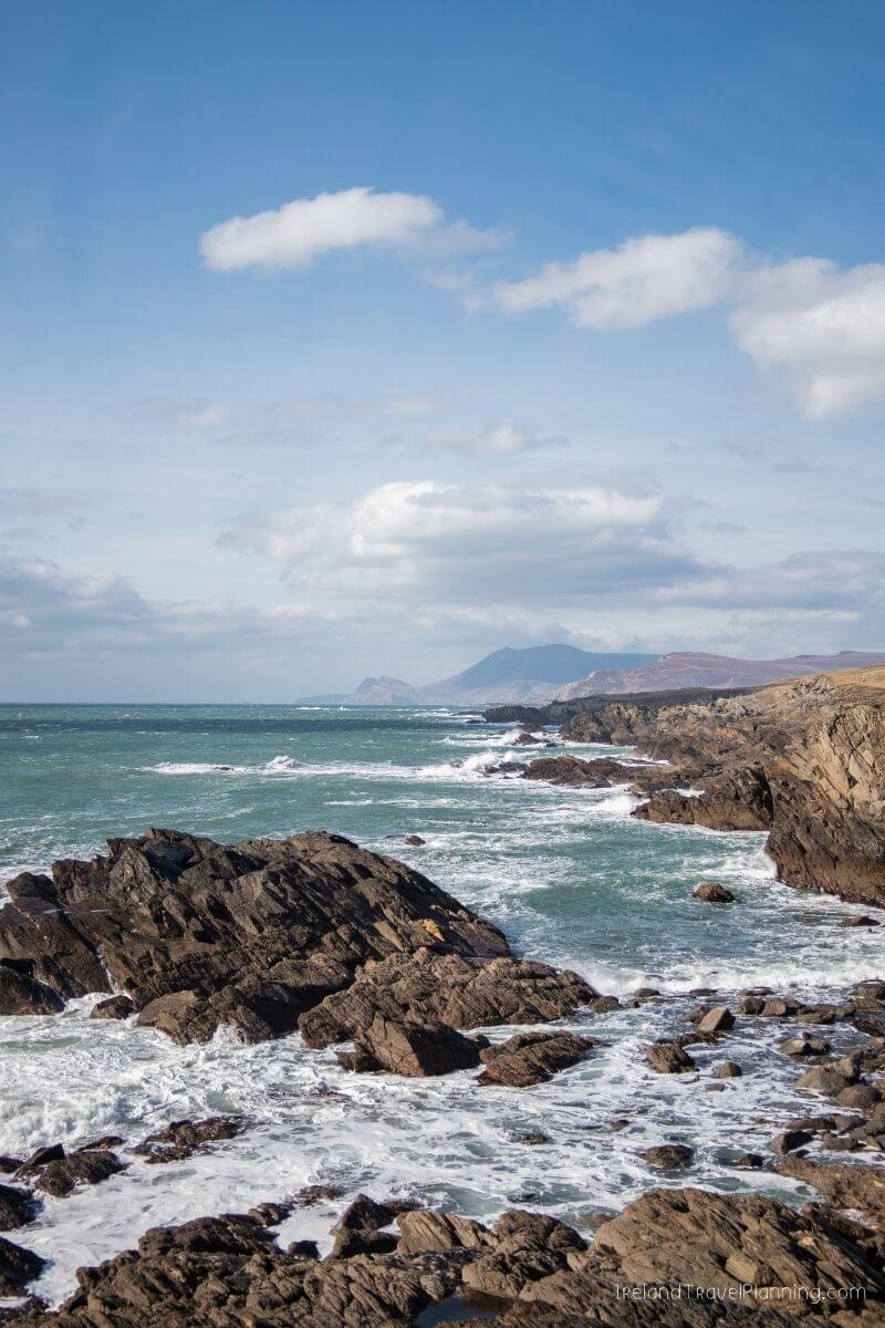 Rugged Irish coastline with waves crashing on rocky shores under a cloudy sky.