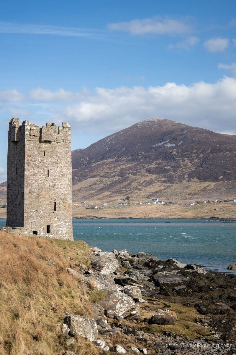 Stone tower on a grassy coastline with a mountain and bay in Ireland