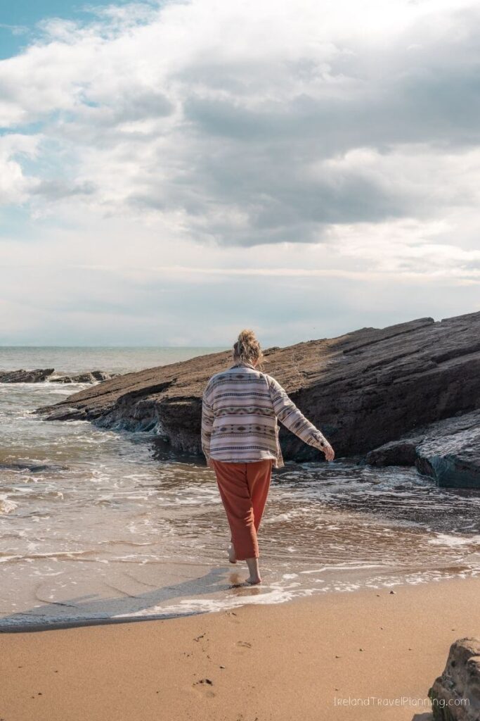 Woman walking into the ocean waves on a rocky Ireland beach