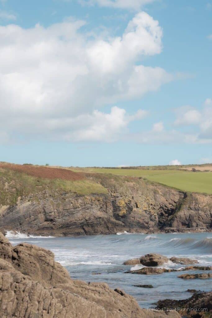 Rugged Irish coastline with waves crashing against cliffs and green fields.
