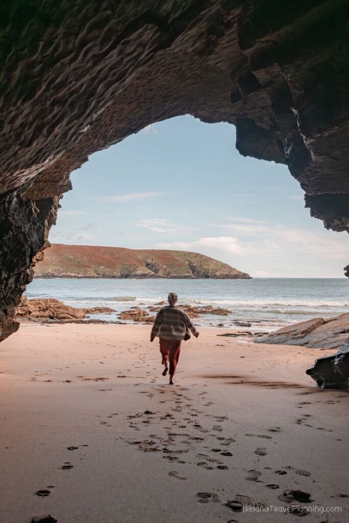 Person running on beach with footprints, ocean and hills in background