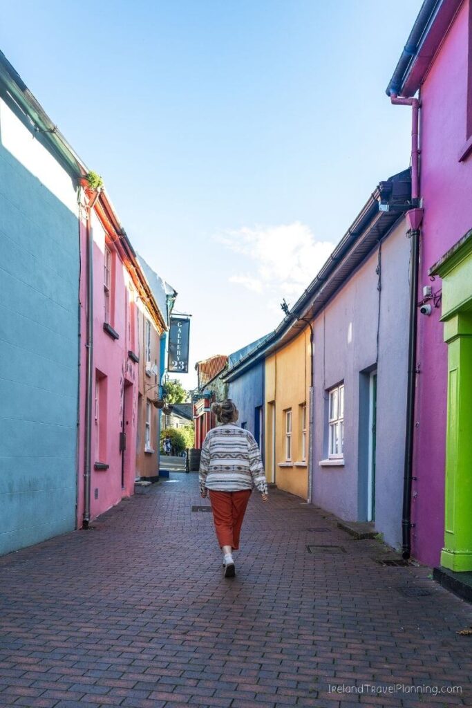 Woman walks down colorful cobblestone alley in Ireland
