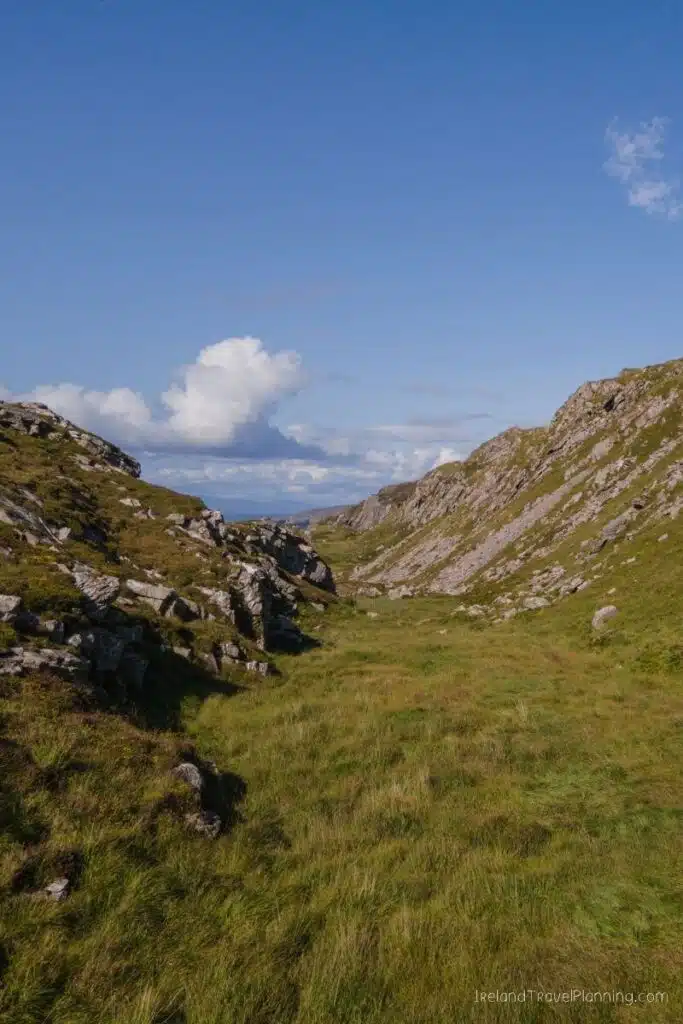 Grassy valley between rocky hills under a blue sky with clouds