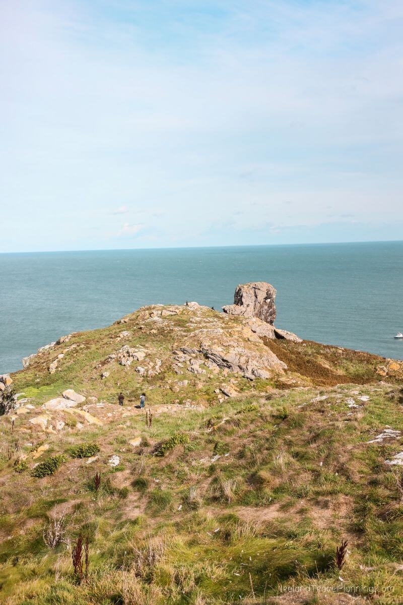 Rocky Irish coastline with hikers on a grassy hill overlooking the sea