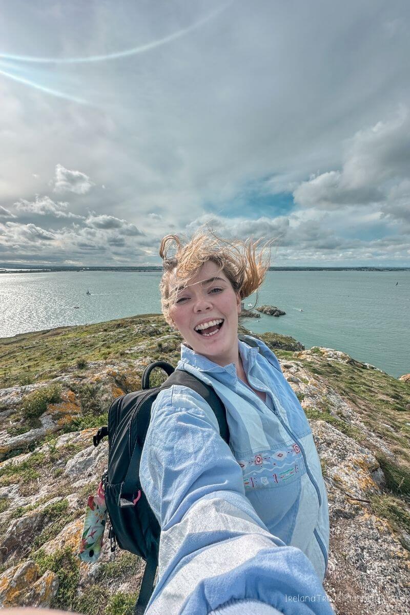 Woman with wind-blown hair smiling on cliff edge in Ireland