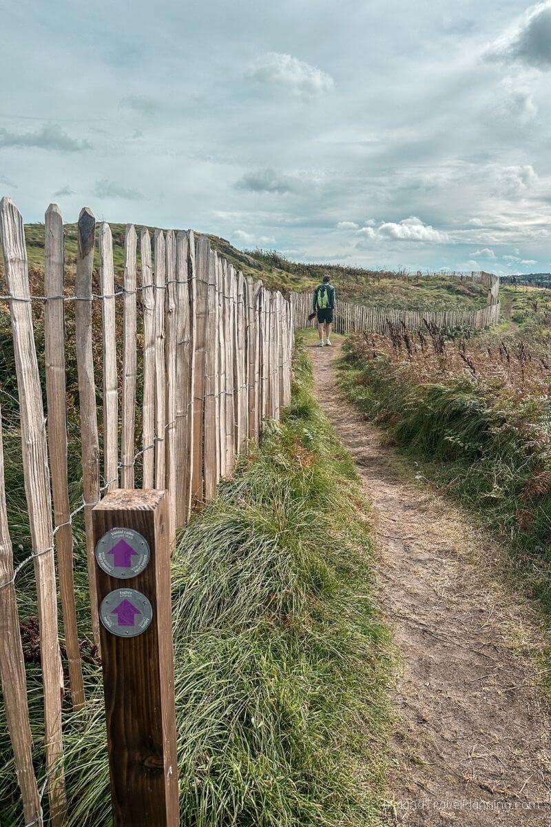 Man walking on a coastal path in Ireland with wooden fence and signage