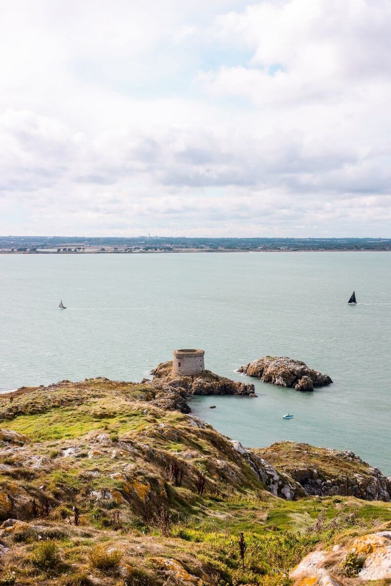 Coastal Ireland: historic tower on rocky outcrop with sailboats in the bay.