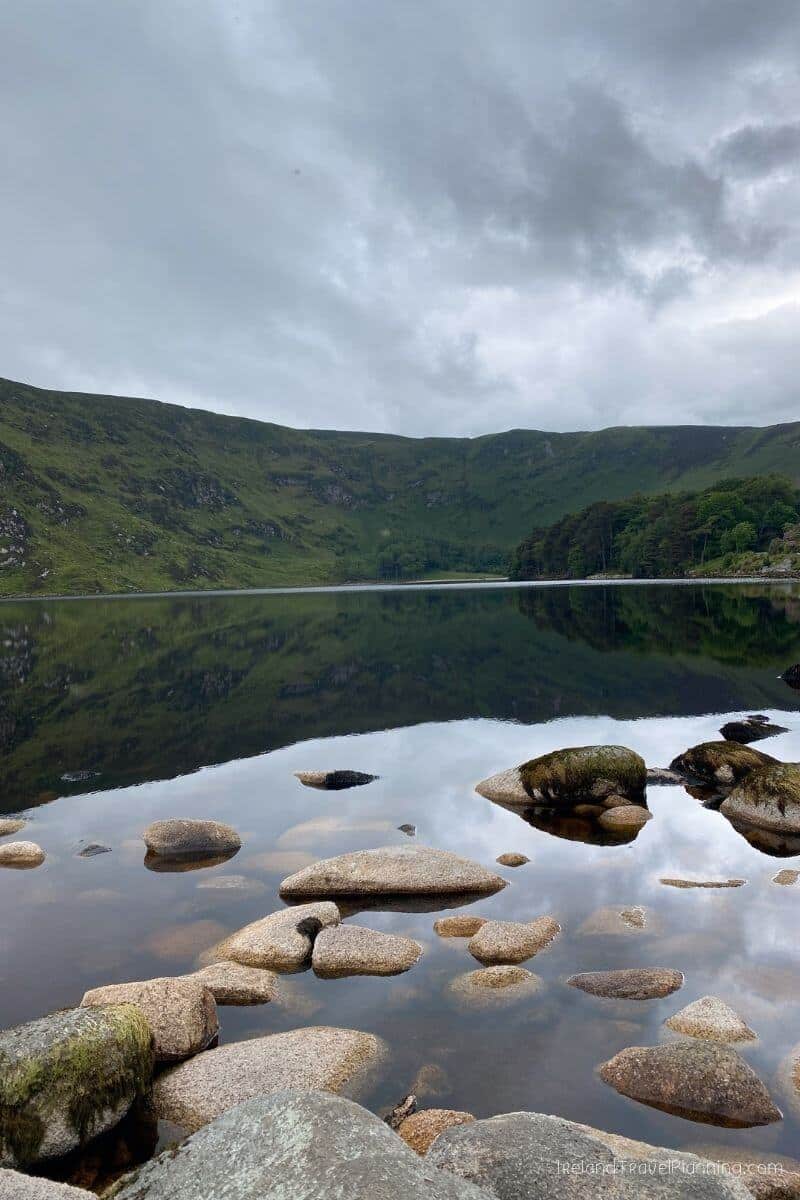 Serene lake and green hills reflecting in calm water, a hidden gem in Ireland.
