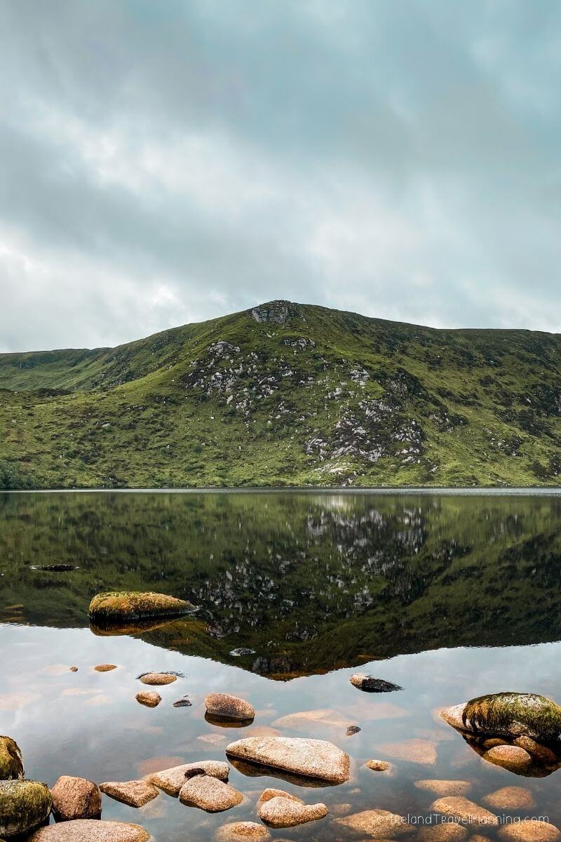 Reflected green Irish mountain and rocky shore of a serene lake