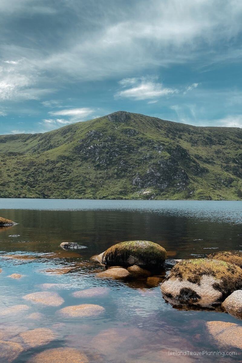 Scenic view of a serene lake in Ireland with a lush green mountain backdrop.