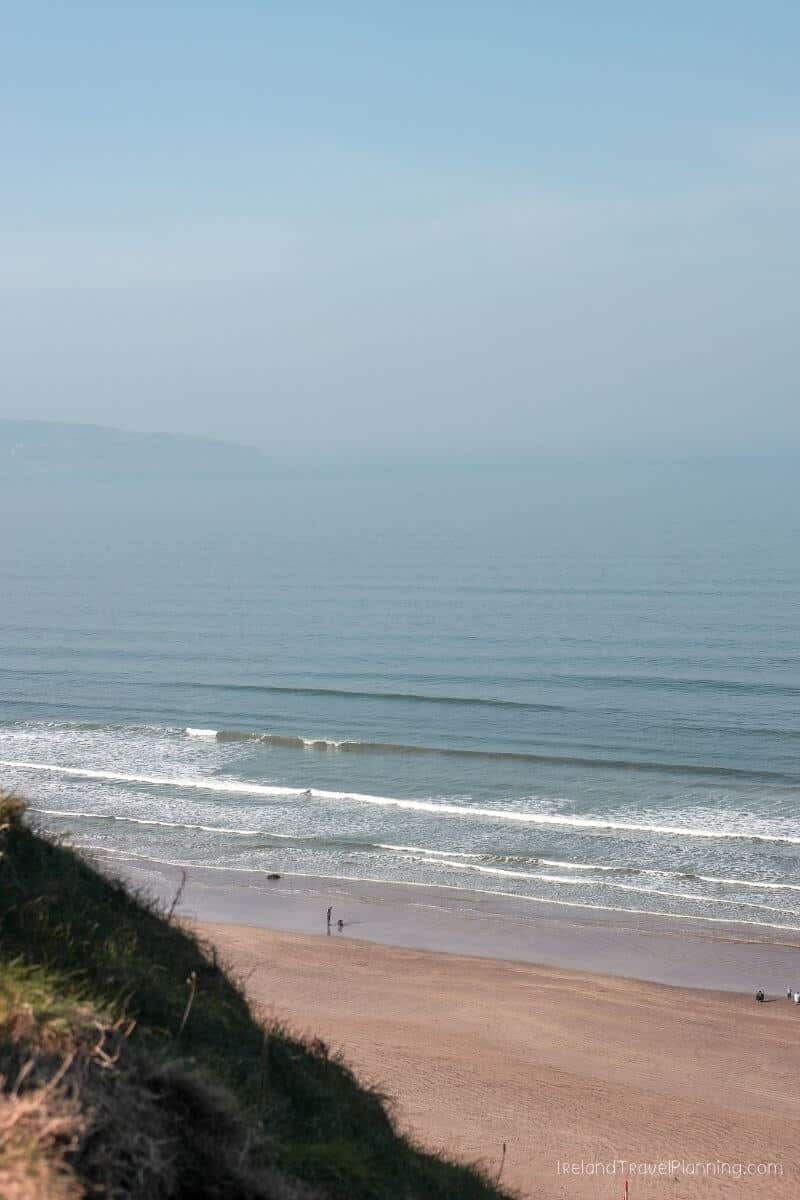 Scenic view of a sandy beach in Ireland with gentle waves and people walking