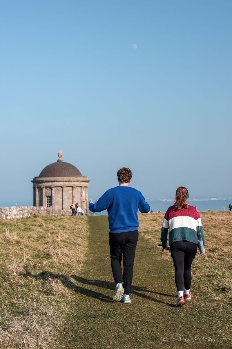 Couple walking towards a historic domed building on a grassy hill in Ireland.