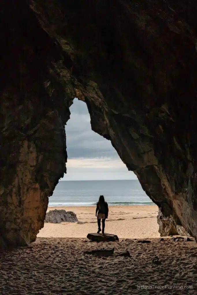 Woman silhouetted in cave mouth looking at beach and ocean